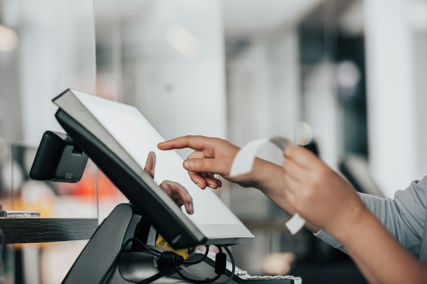 Mani di una cassiera sullo schermo touch della cassa, con lo scontrino appena stampato